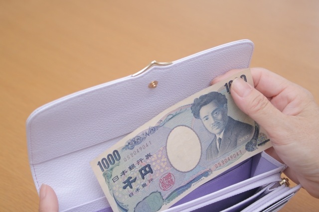 白い長財布に千円札を丁寧に差し込む手元のクローズアップ写真